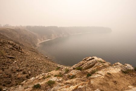 Lake Baikal in the fog in the morning. Shot from a high cliff. Ripples on the water. Selective focus on the front stones. Copy space.の写真素材