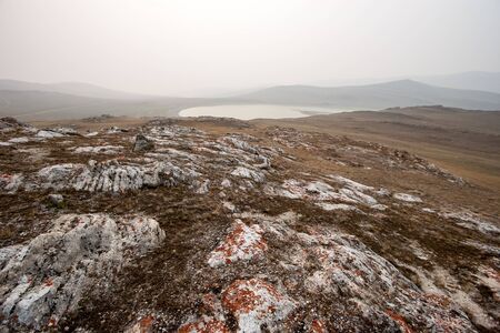 Beautiful steppe landscape with stones, hills and a lake in the fog in the morning. Red stones with moss. Like a lunar landscape. Copy space.の写真素材