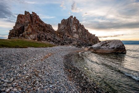 View from the pebble shore to the rock Shamanka from the island of Olkhon on Lake Baikal. The waves are small. Sunset light behind the rock. Clouds in the sky.の写真素材