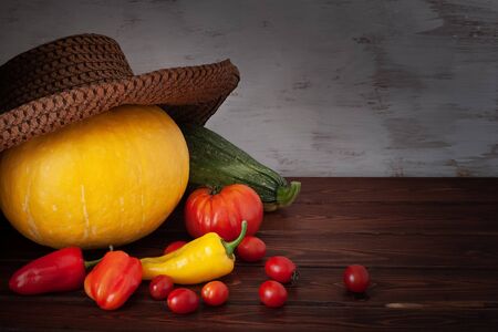 Pumpkin in a hat, zucchini with scattered tomatoes and peppers on the boards. The boards are brown, the background is carelessly painted with white paint. Vignette.の写真素材