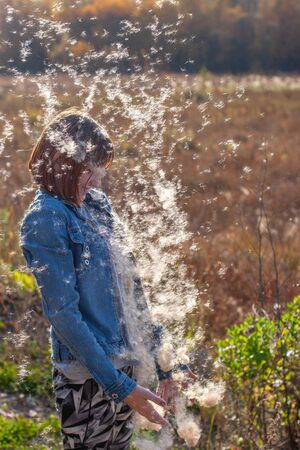 Fluff from cattail falls next to a teenager who looks at him. Fluff glistens in the sun. The...