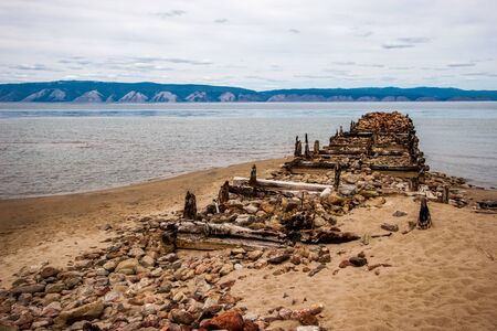The destroyed old pier on the island of Olkhon on Lake Baikal. On the shore of stones and sand. Behind the mountain lake.の写真素材