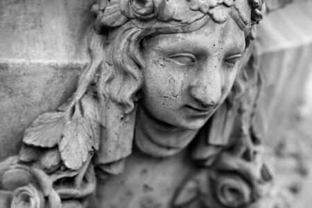 Vintage plaster face of a young woman with leaf hair on the wall. Cracked sculpture with roughness and cracks. Black and white photography.の写真素材