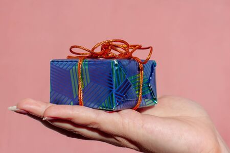 A gift tied with an orange rope lies on a female hand. The packaging is blue with green. Pink background.の写真素材