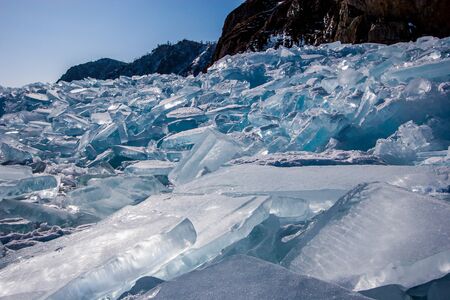 Many storm-broken pieces of ice in a large heap next to the rock. Sunny day, ice glistens in the...