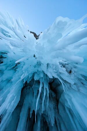 Blue long icicles hanging from the cave arches. Winter stalactites. Copy space in the blue sky....