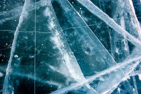 The natural texture of the transparent ice of Lake Baikal with deep cracks. Beautiful winter background.