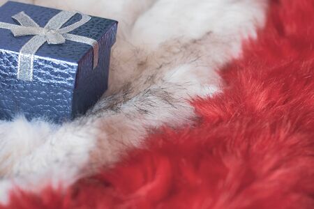 Blue gift box with a bow on fluffy white and red fur. Selective focus on the box with a bow. Copy space.の写真素材