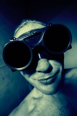 Smiling guy in big dark welding glasses. Looks like huge eyes. Dark blue tinted. Selective focus.の写真素材