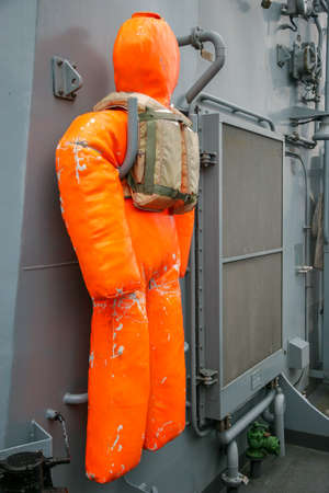 A training mannequin hangs on the wall of a warship. Orange doll with a vest. Shabby mannequin.