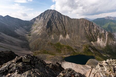 View from the cliff to the opposite mountain and a small lake in front of it. Green mountain ranges...