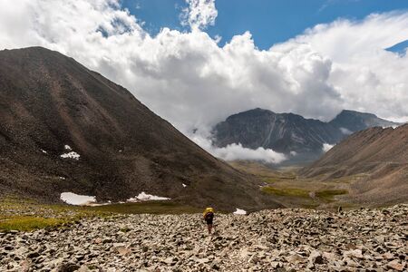 Hiker man with a backpack is walking among the high mountains on stones on the ground. High...