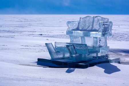 Sled from ice on a pedestal on the lake Baikal. Ice sculpture. The ice of the lake is covered with snow. Sunny. Horizontal.の写真素材