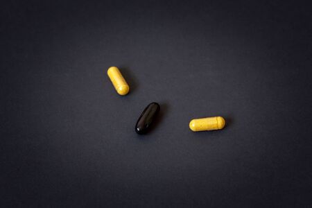 Three pills in capsules on a dark background. Yellow and black tablets. Vignetting. Horizontal.