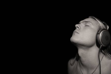 Young guy enjoys listening to music in big headphones. Eyes closed. Copy space. Isolated on a black background. Horizontal.の写真素材