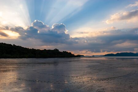 Beautiful sunset at sea at low tide. The rays of the sun from behind the clouds. Dark silhouette of...