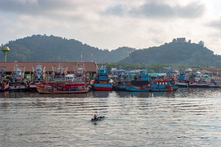 Thailand - January 31, 2018: Many fishing boats stand near the shore and one very small boat floats along the river. A man is rowing with one oar. Horizontal.のeditorial素材
