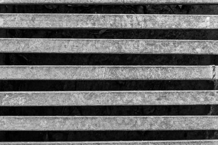 Black and white photo of an iron grate over a drainage channel on the road. Rusty texture on metal. Horizontal.の写真素材