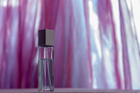 A faceted perfume bottle stands on a blurred background of fabric. Glass vial with a metal cap. Blank for mock up. Shallow depth of field. Horizontal.の写真素材