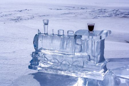 Ice sculpture in the form of a train locomotive and red liqueur in a glass. Ice dissolves in the...