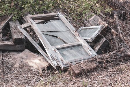 Old window frames with broken glass and thick wooden beams lie on the ground. Glasses are dirty. Around the withered grass. Horizontal.の写真素材