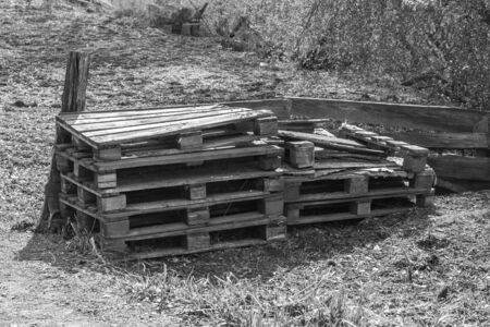 Old curves and broken pallets lie on the grass by the fence. Sunny. Black and white photo. Horizontal.の写真素材