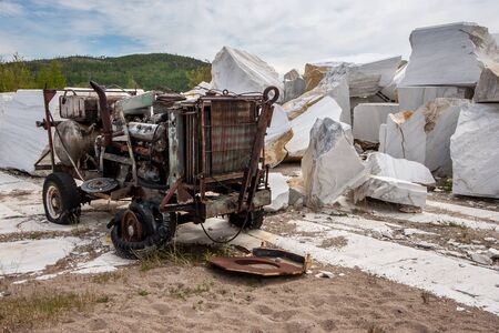 Old soviet broken rusty compressor in an abandoned marble quarry. A pile of large marble stones. A pile of sand in the foreground. Cloudy. Horizontal.の写真素材