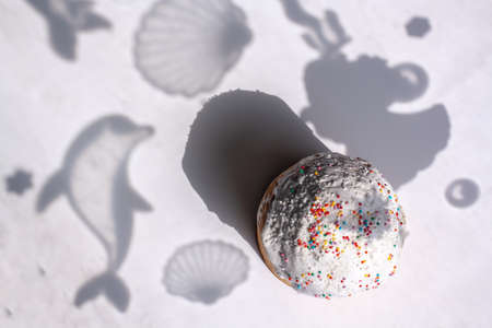 Easter cake in flat lay style with shadows of dolphin and shells on the background. Traditional food for Easter holiday in Russia. White icing with small colored balls. Horizontal.の写真素材