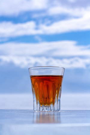 Chilled whiskey in a glass stands on an ice surface against a blurry sky. Orange alcoholic drink in a glass. Copy space. Side view. Vertical.の写真素材