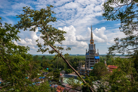 Tall Buddhist temple with spire Tiger Cave in Krabi province in Thailand through trees. Blue sky with clouds.の写真素材
