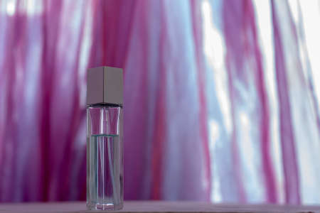 A long perfume bottle stands against a blurred pink fabric. Glass vial with a metal cap. Blank for mock up. Shallow depth of field. Horizontal.の写真素材