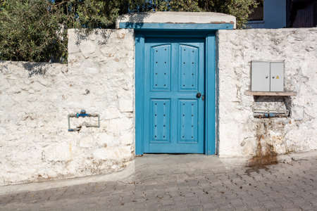 Blue wooden door in old stone wall. Tubes and an electric board stick out.