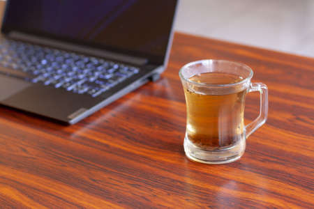 Tea mug with selective focus and laptop on blown table.の写真素材
