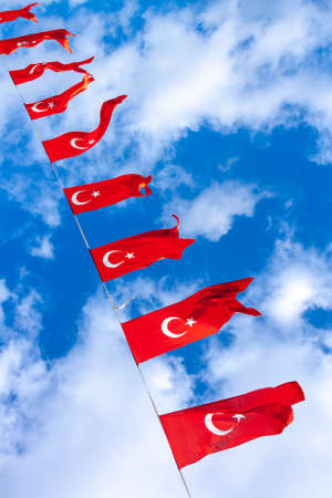 Many Turkish national flags on rope against background of blue sky and clouds.の写真素材
