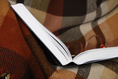 Open book and spectacles lying on chequered plaidの写真素材
