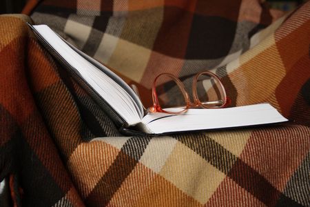 Open book and spectacles lying on chequered plaidの写真素材