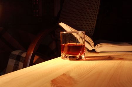 Glass of drink on wooden table on backgound with open book and home interiorの写真素材