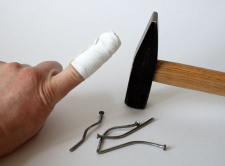 Male hand with bandaged finger on background with hammer and nails