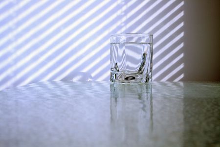 Glass of cold clear water standing on glass table on background with jalousie shadowの写真素材