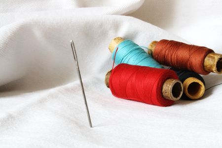 Steel needle standing on background with spools of the multicoloured thread