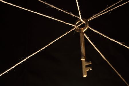 Yellow brass key hanging on ropes on dark backgroundの写真素材