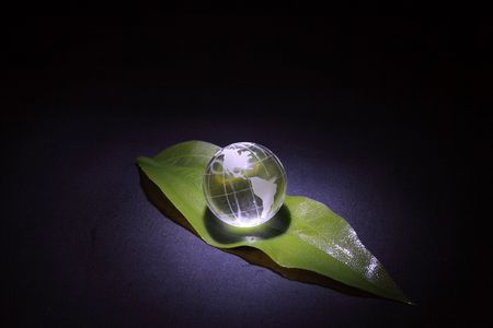 Little glassy globe lying on green leaf on dark backgroundの写真素材