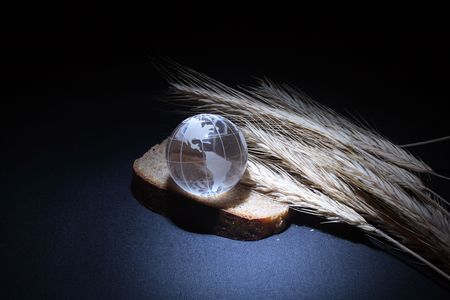 Little glassy globe with rye bread and wheat ears on dark backroundの写真素材