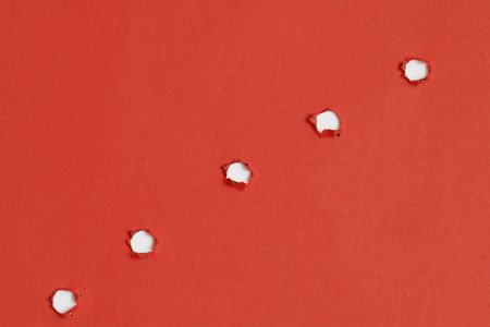 Red papery background with five bullet holesの写真素材