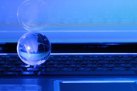 Blue background with glassy globe lying on laptop keyboardの写真素材