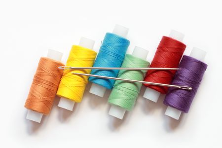 Spools of variegated thread with needles lying on white background
