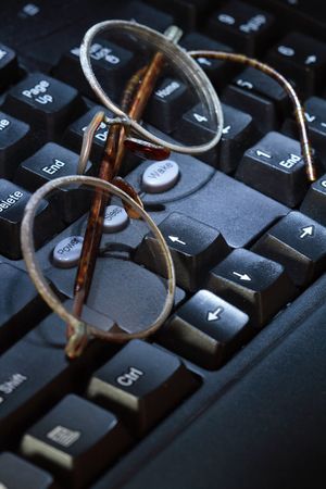 Old spectacles lying on modern black computer's keyboardの写真素材