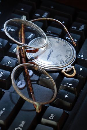 Old spectacles and watch lying on modern black computer's keyboardの写真素材