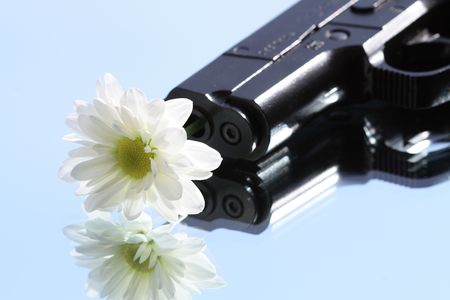 Black modern automatic pistol with flower isolated on blue sky backgroundの写真素材
