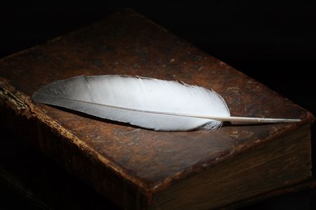 Dark background with feather lying on antique bookの写真素材
